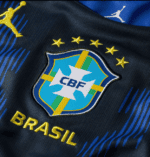 Close-up of Brazil national football jersey showing the CBF crest, four gold stars, and 'BRASIL' text on dark fabric with blue and green accents.