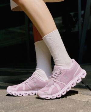 Person wearing light pink athletic sneakers and white crew socks, standing on a sunlit pavement.