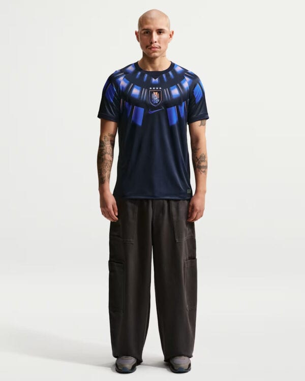 Man wearing a navy blue athletic jersey with crest, paired with black cargo pants and sneakers (front view).