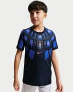 Young boy wearing a dark blue soccer jersey with a crest and blue stripes on the chest area.
