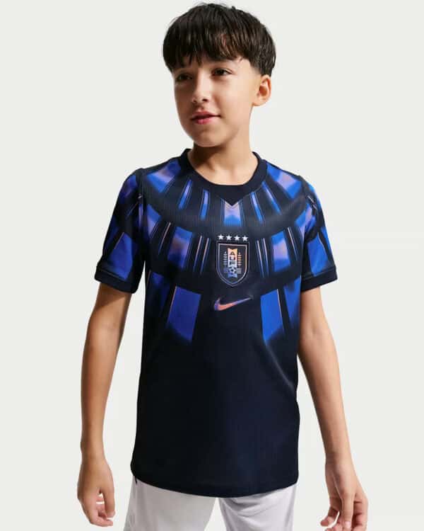 Young boy wearing a dark blue soccer jersey with a crest and blue stripes on the chest area.