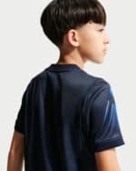 Side profile of a young boy wearing a navy athletic shirt, seen from the back-right against a light background.
