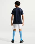 Back view of a young boy wearing a navy soccer jersey, white shorts, bright blue knee-high socks, and black cleats.