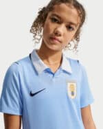 Young girl wearing a light blue soccer jersey with a crest and Nike logo, looking at the camera.