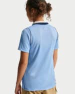 Person seen from behind wearing a light blue polo shirt with dark collar trim and tan shorts; curly hair tied up.