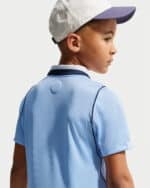 Side profile of a young boy wearing a light blue polo shirt and a white cap with a purple brim