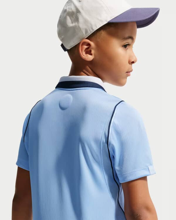 Side profile of a young boy wearing a light blue polo shirt and a white cap with a purple brim