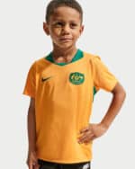 Young boy wearing an orange Australia soccer jersey with green collar and crest, standing with hand on hip.