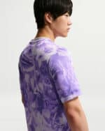 Side profile of a young man wearing a lavender-purple camo-pattern athletic shirt.