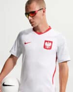 Male model in a white Poland national team soccer jersey with red crest, holding a white soccer ball and wearing sporty sunglasses