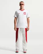Male model in a white Poland national team jersey with red crest and red trim, paired with white pants with red side panels.