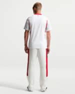 Back view of a man wearing a white athletic jersey with red trim and white pants with red side panels, facing away