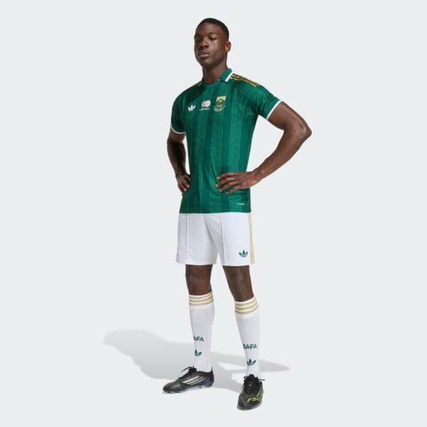 Soccer player in a green striped jersey and white shorts standing with hands on hips, facing camera slightly to the left.