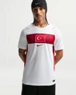 Male model wearing a white Nike athletic jersey with a red chest band and Turkish flag, against a light background, wearing a black beanie.