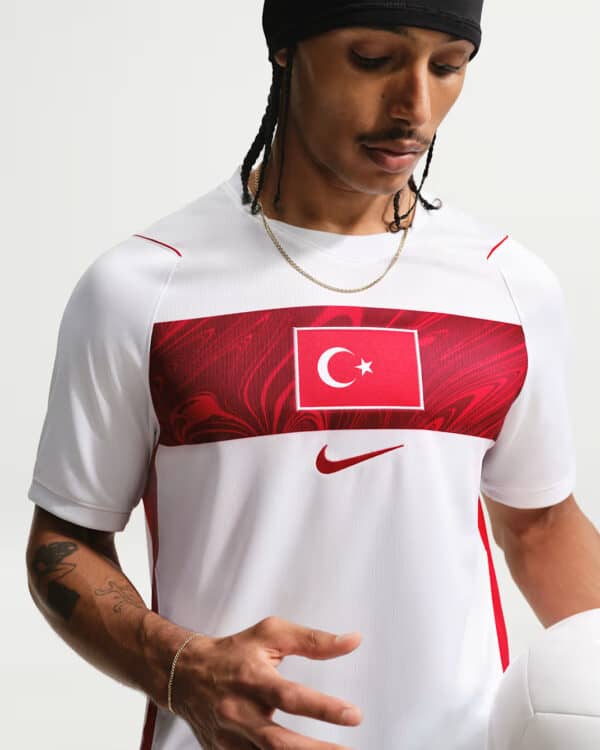 Athlete in a white soccer jersey with a red Turkish flag panel, holding a soccer ball.