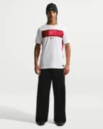 Male model wearing a white athletic shirt with a red Turkish flag stripe across the chest, black wide-leg pants, and a black beanie.