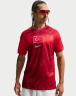 Man wearing a red athletic shirt with a Turkish flag patch and Nike swoosh, plus red wraparound sunglasses, looking to the side.