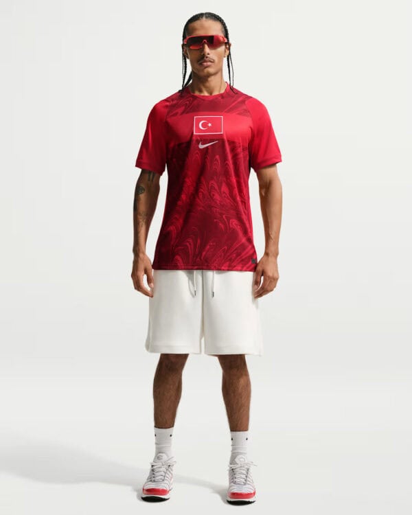 Athlete wearing a red Turkish-flag jersey, white shorts, and white sneakers, standing with hands at sides.
