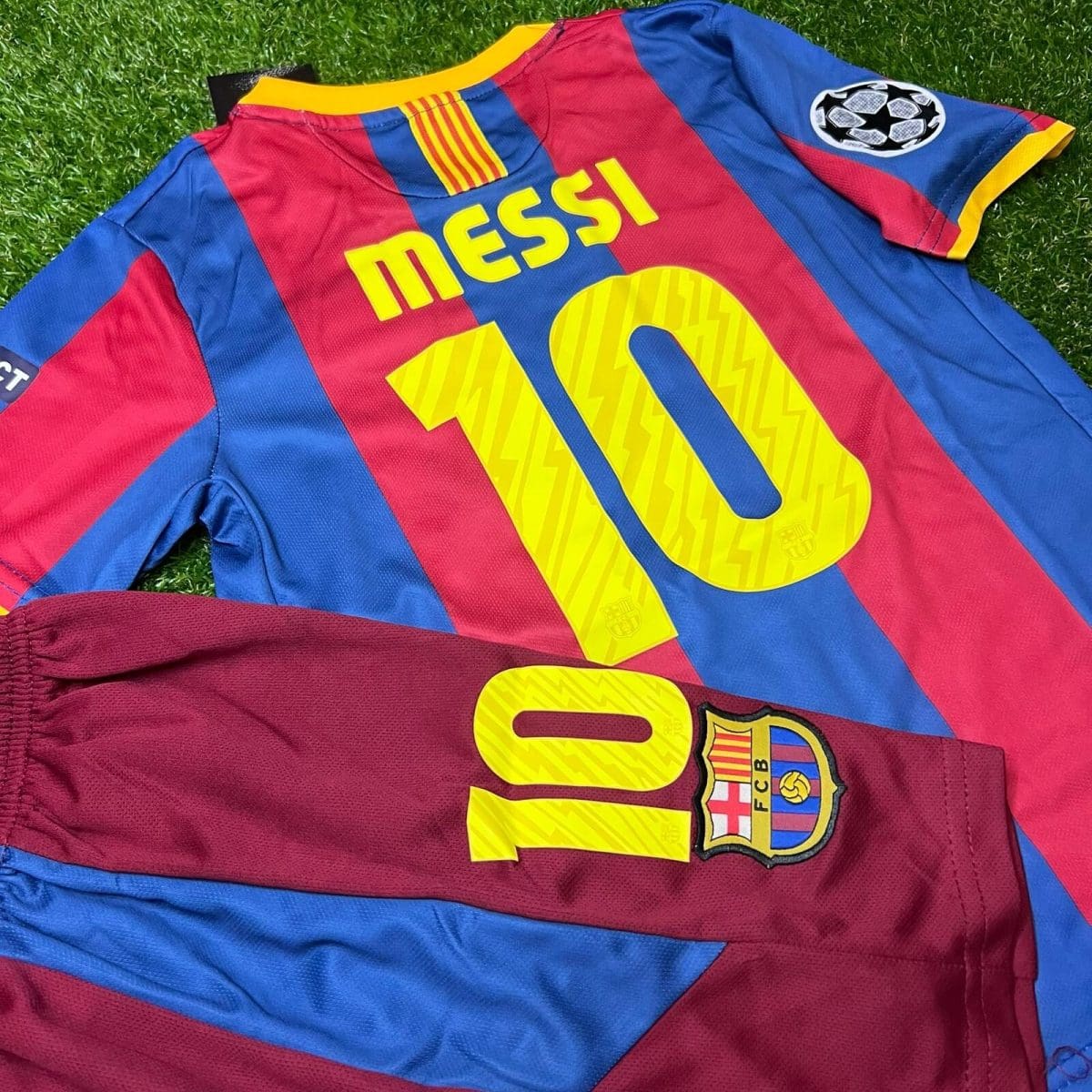 Barcelona football jersey laid on grass featuring 'MESSI 10' in bold yellow letters with a Champions League patch on the sleeve.