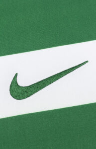 Close-up of a green Nike swoosh embroidered on white fabric with green diagonal stripes in the background.