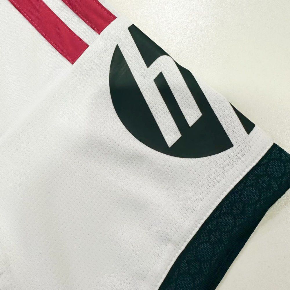 00143f52-923b-4700-b4e0-7bffb5016596 | UAE SPORT STORE Close-up of a white sports jersey with red stripes near the shoulder and a large black circular logo on the sleeve.