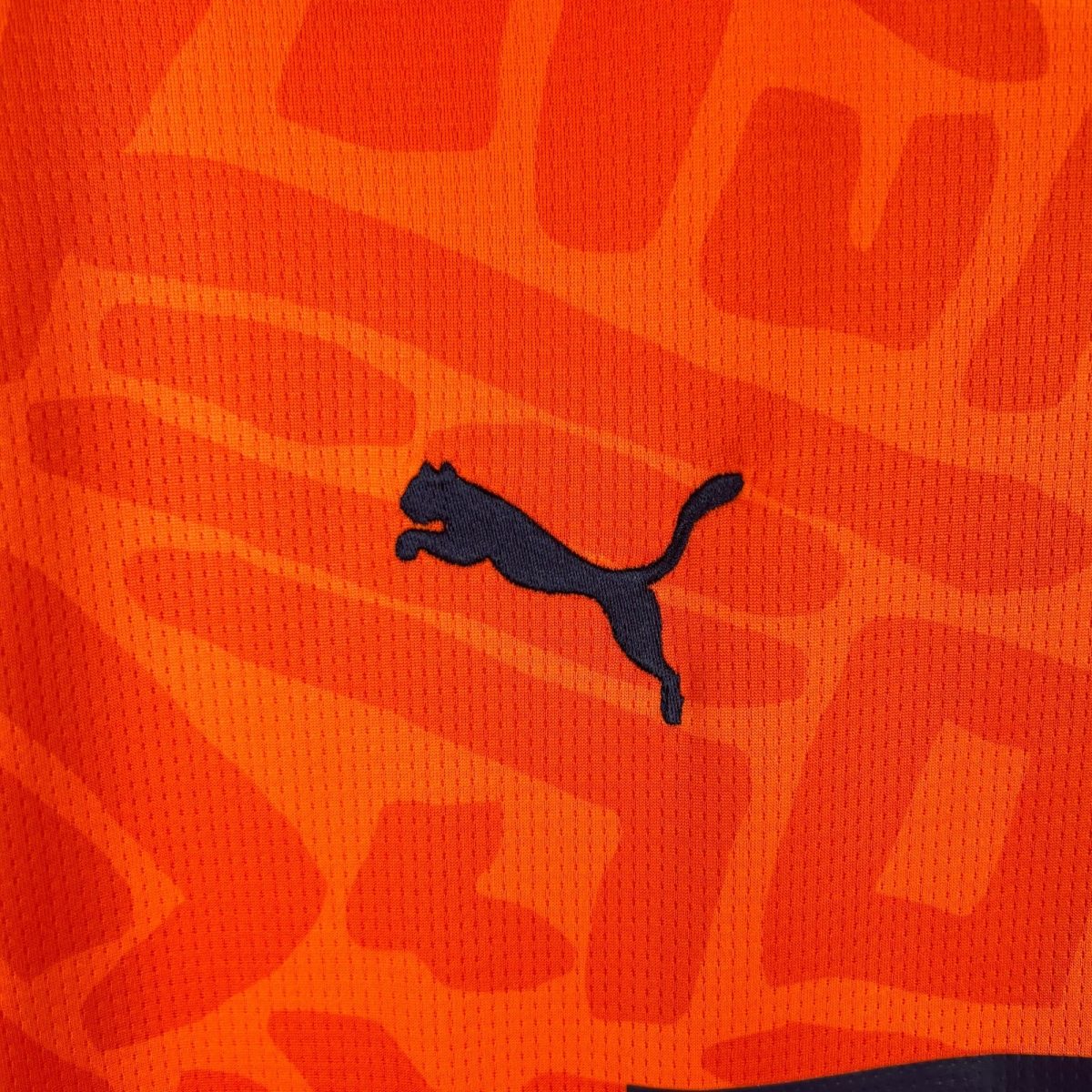 Close-up of orange fabric with a dark blue Puma logo visible on the right edge.