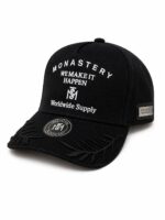 Black baseball cap with white embroidered text reading 'MONASTERY WE MAKE IT HAPPEN Worldwide Supply' and decorative brim embroidery on the bill.