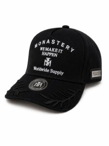 Black baseball cap with white embroidered text: 'MONASTERY WE MAKE IT HAPPEN Worldwide Supply' and decorative stitched brim detail
