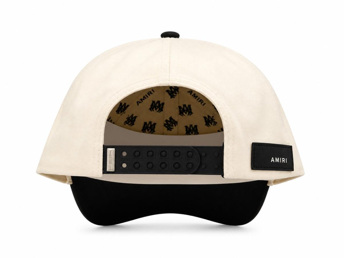 Back view of a beige Amiri cap with a black plastic snap closure and a small Amiri patch on the side, brim underneath in black.