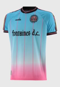 00A469D7-5523-4E43-A494-661921412247 | UAE SPORT STORE Light blue to pink gradient soccer jersey with pink vertical stripes, Fontaines D.C. sponsor text, and club crest on the chest.