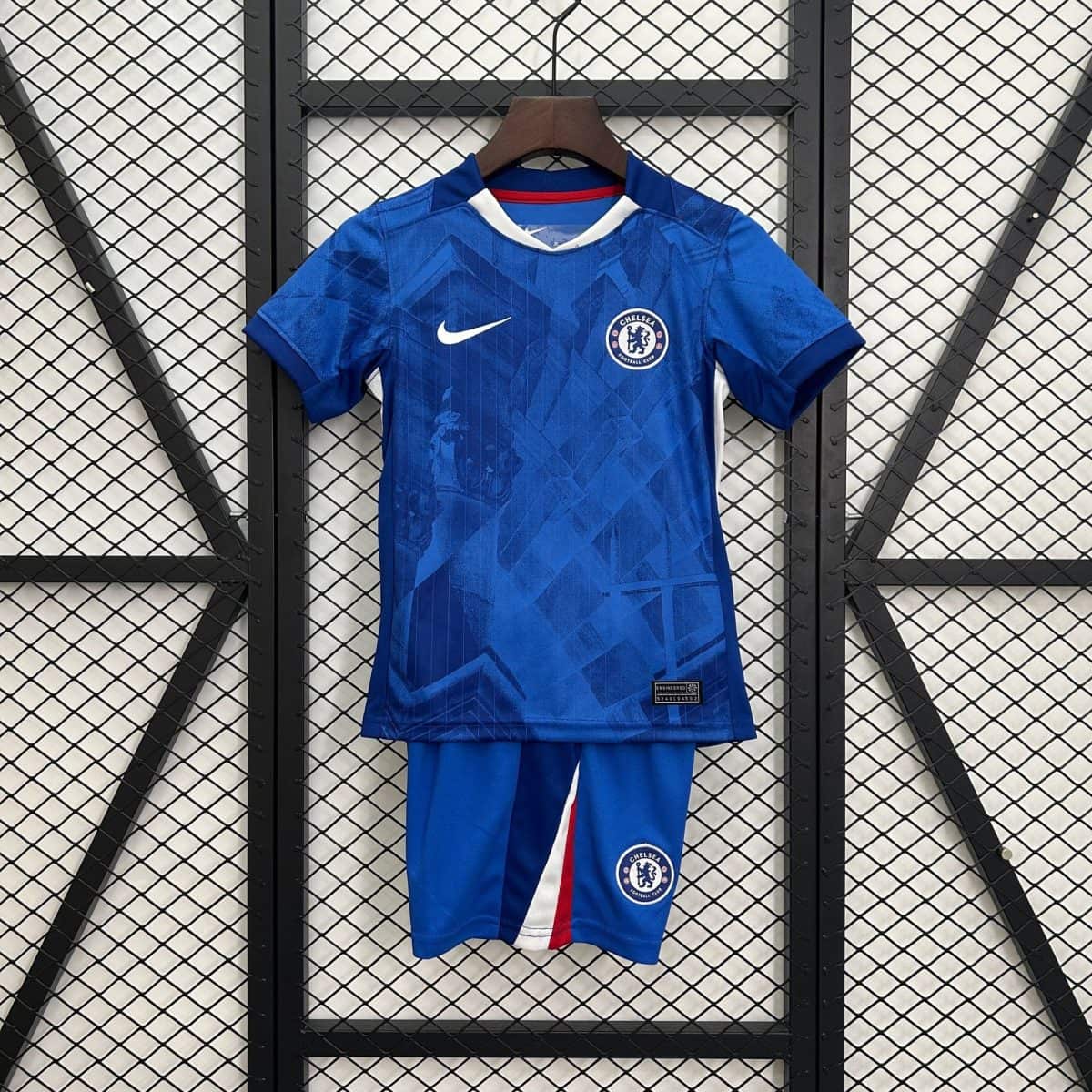 Chelsea football jersey on a wooden hanger against a metal grid background, featuring a white Nike swoosh and Chelsea crest on a blue kit with red/white trim.