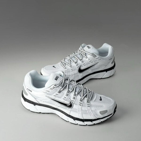 Pair of white Nike running shoes with a black swoosh on a gray backdrop.