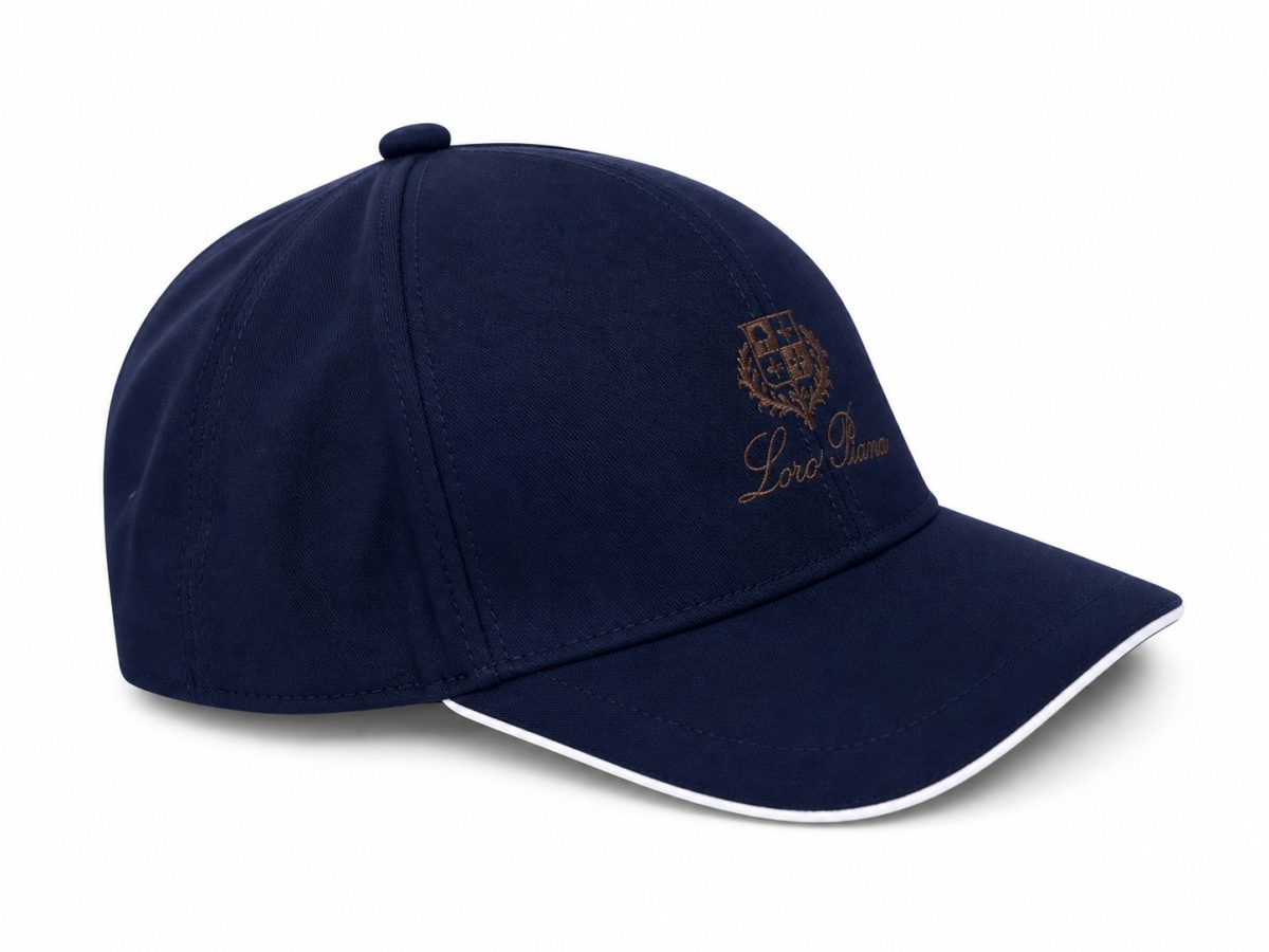 Navy baseball cap with an embroidered crest and cursive text on the front panel, white-trimmed brim visible to the side of the image.