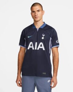 Man wearing a navy Tottenham Hotspur football jersey with the AIA sponsor and blue collar, standing against a light background.