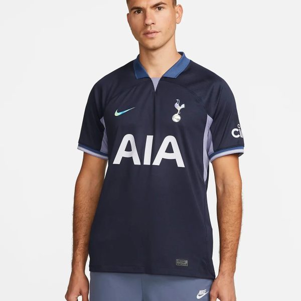 Man wearing a navy Tottenham Hotspur football jersey with the AIA sponsor and blue collar, standing against a light background.