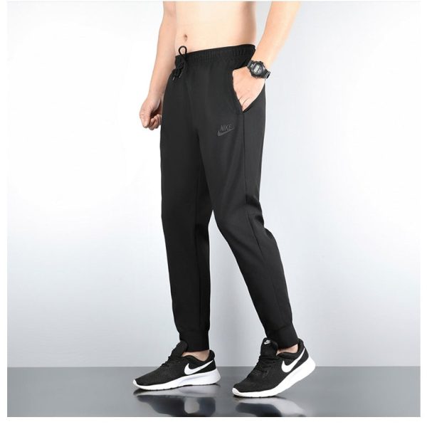 Person wearing black Nike joggers with a drawstring, hands in pockets, black Nike sneakers with white Swoosh.