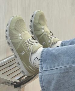 Beige athletic sneakers with chunky gray soles, white laces, worn with light-wash jeans and socks featuring a smiley face.