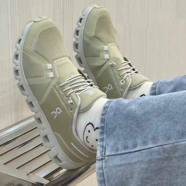 Beige athletic sneakers with chunky gray soles, white laces, worn with light-wash jeans and socks featuring a smiley face.