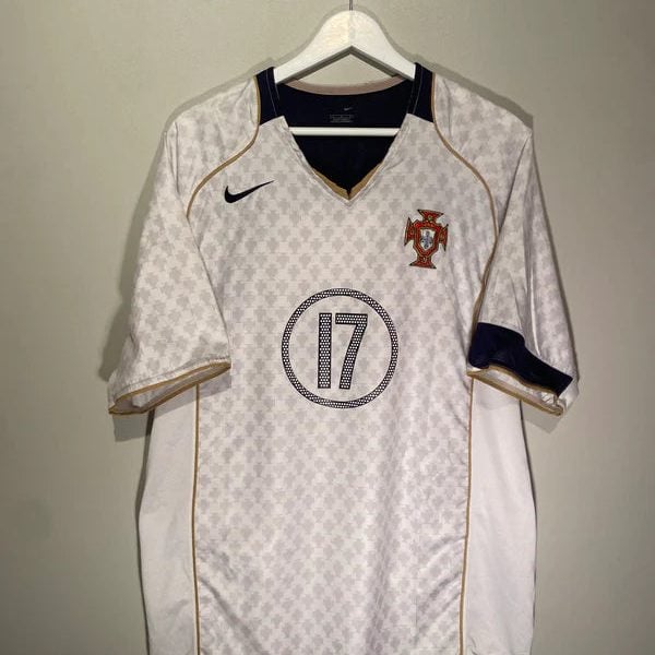 Portugal national team white soccer jersey with gold piping and crest on the left chest, hanging on a hanger.