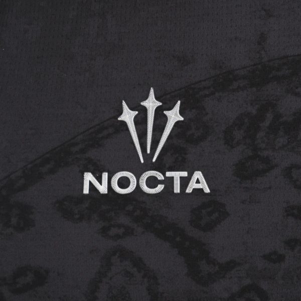 White Nocta logo (three prongs) with the word NOCTA embroidered on dark patterned fabric