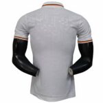 Back view of a white polo shirt with black-and-orange trim on the sleeves and collar, featuring a subtle geometric pattern.