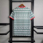 Back of a white T-shirt with green geometric pattern, red collar and cuffs, hanging on a wooden hanger in a black metal rack.