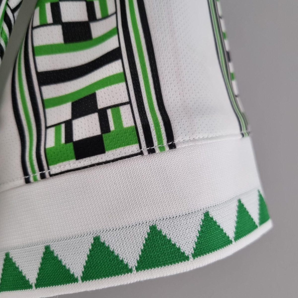 Close-up of white fabric with bold green and black geometric print, showing stitching edge of a textile item like a sports jersey.
