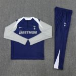 Tottenham training kit laid flat: blue long-sleeve top with gray sleeves, white shoulder panels, Nike swoosh, club crest, BetMGM sponsor, plus matching blue pants with Spurs crest.