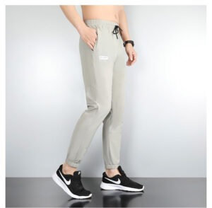 Side view of light gray drawstring jogger pants with elastic cuffs, worn with black-and-white sneakers by a person cropped at the waist.