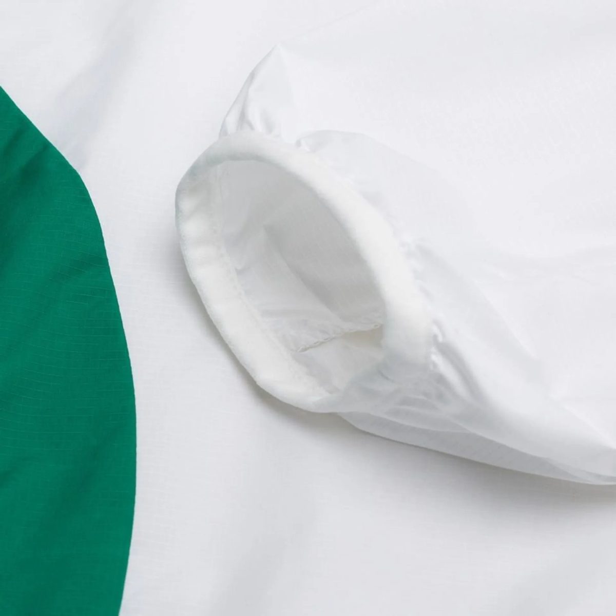 Close-up of a white folded napkin on a white surface with a green curved edge on the left side.