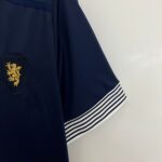 Close-up of a dark navy blazer sleeve with a gold embroidered crest patch visible near the chest area against a light wall.