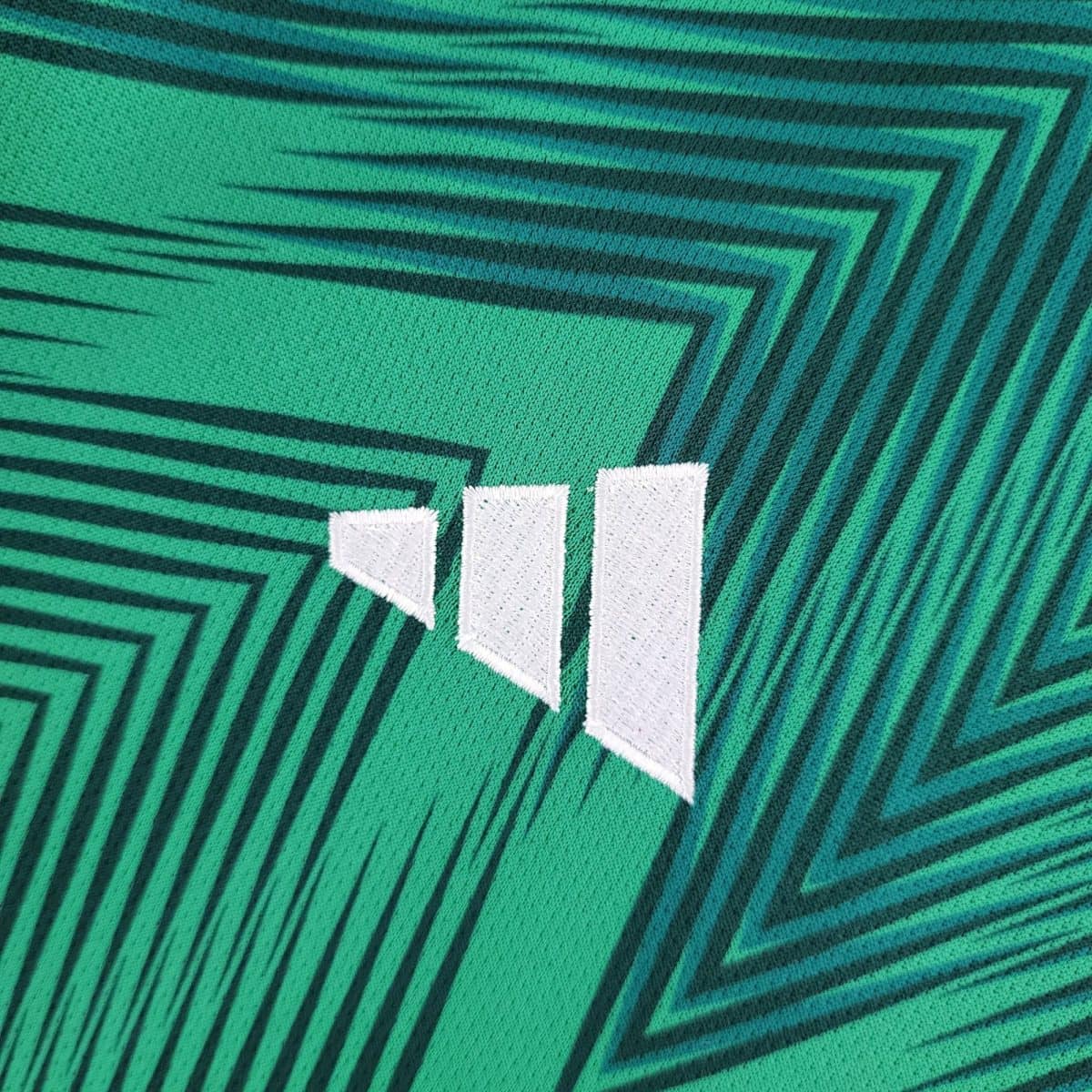 Close-up of green fabric featuring a teal angular chevron pattern and white stitched blocks in the foreground.