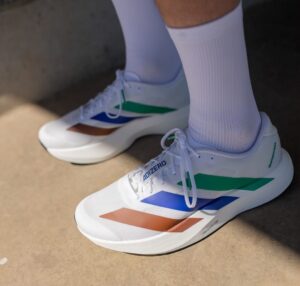 White Adizero running shoes with blue, green, and orange stripes worn with white socks