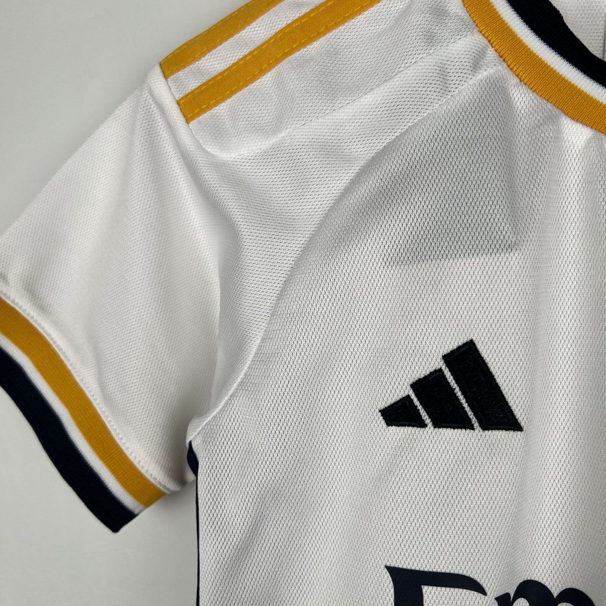 Close-up of a white mesh sports jersey with yellow trim and partial black lettering/logo edge.